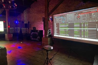 Salle en pierre avec éclairage tamisé, écran de projection affichant une interface de logiciel DJ et matériel audio installé.
