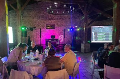 Des convives dînent à des tables rondes dans une salle en pierre avec éclairages colorés et matériel de DJ en arrière-plan.
