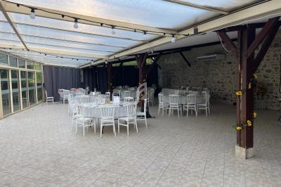 Salle de réception couverte avec tables et chaises blanches, décorée de tournesols, murs en pierre apparente.