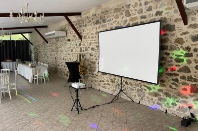 Salle en pierre avec un écran de projection, un vidéoprojecteur et des tables dressées pour un événement.
