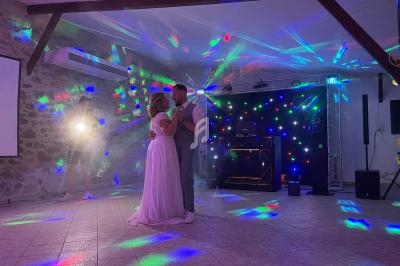 Un couple danse sous des lumières colorées dans une salle avec un décor en pierre et un équipement de DJ en arrière-plan.