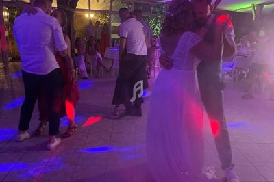 Un couple danse sous des lumières colorées dans une salle de réception, entouré de quelques invités.