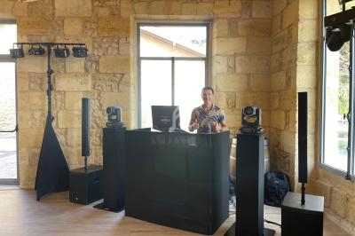 Un DJ se tient derrière une table équipée de matériel audio et d'éclairage dans une salle en pierre lumineuse.