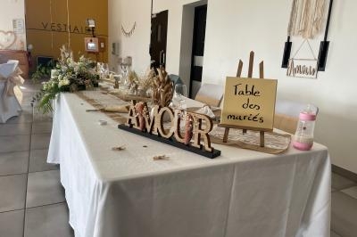 Table décorée pour les mariés avec fleurs, panneaux ’Amour’ et ’Table des mariés’, dans une salle de réception.
