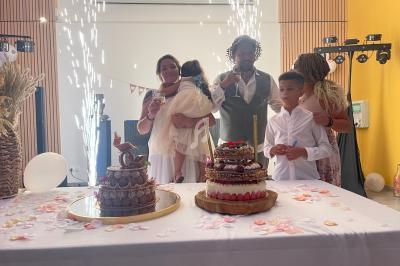 Des personnes rassemblées autour d'une table décorée avec des gâteaux et des pétales, dans une ambiance festive.