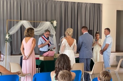 Un mariage civil avec un officiant, des mariés et des témoins dans une salle décorée de fleurs et de voilages.