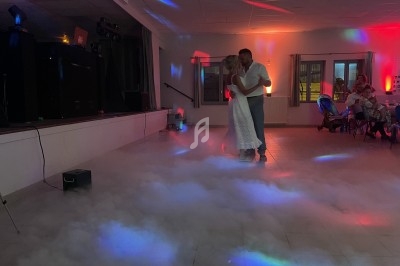 Un couple danse dans une salle éclairée par des lumières colorées, entouré d'un effet de fumée au sol.