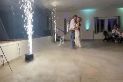 Un couple danse dans une salle éclairée, entouré de fumée au sol et de jets d'étincelles.