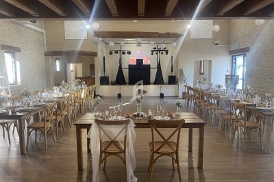 Salle de réception décorée pour un événement, avec tables dressées, chaises en bois et espace pour une piste de danse.