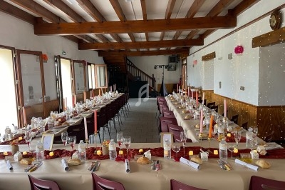 Salle décorée pour un repas festif avec deux longues tables dressées, bougies et chemins de table rouges.