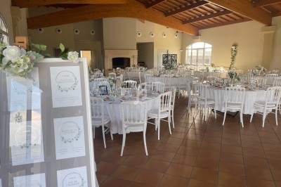 Salle de réception lumineuse avec tables rondes dressées, chaises blanches et décoration florale élégante.
