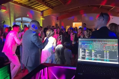 Groupe de personnes dansant lors d'une fête, éclairées par des lumières colorées, avec une table de DJ au premier plan.
