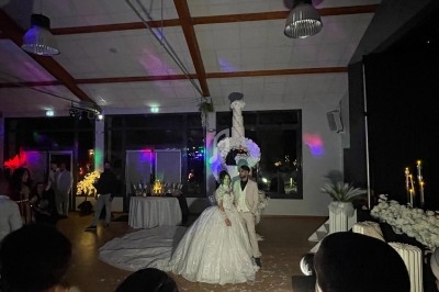 Un couple en tenue de mariage pose dans une salle décorée avec des lumières colorées et des fleurs blanches.