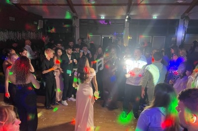 Groupe de personnes dans une salle de fête, éclairée par des lumières colorées, avec une femme en robe claire au centre.
