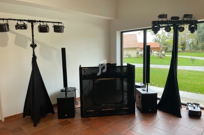 Équipement de sonorisation et d'éclairage installé dans une salle avec vue sur un jardin à travers une baie vitrée.