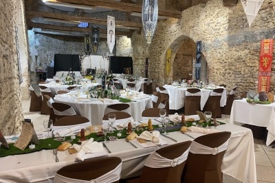 Salle de réception décorée dans un style médiéval avec tables dressées, nappes blanches et murs en pierre apparente.
