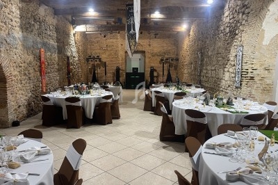Salle en pierre avec des tables rondes dressées pour un repas, éclairage chaleureux et décoration sobre.