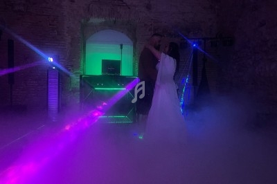 Un couple danse dans une ambiance tamisée avec des lumières colorées et de la fumée dans une salle en pierre.