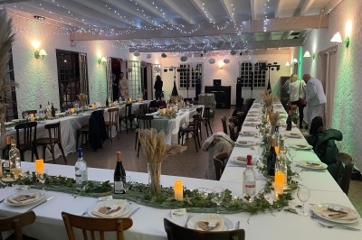 Salle de réception décorée pour un dîner, avec longues tables ornées de bougies, feuillages et vaisselle élégante.
