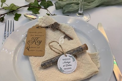 Assiette avec une serviette en tissu, une clé ancienne, un tube en verre et une étiquette de mariage, sur une table décorée.