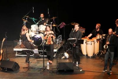 Un groupe de musiciens joue sur scène avec divers instruments, dont une batterie, des guitares et des percussions.