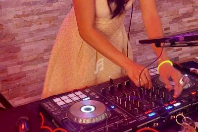 Femme en robe claire mixant de la musique sur une table de mixage avec des lumières colorées en arrière-plan.