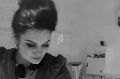 Femme aux cheveux relevés, regard baissé, dans une pièce au décor sobre et éclairage tamisé.