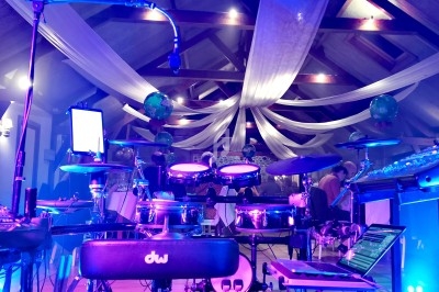 Vue d'une scène musicale avec une batterie électronique, des équipements audio et un éclairage coloré dans une salle décorée.