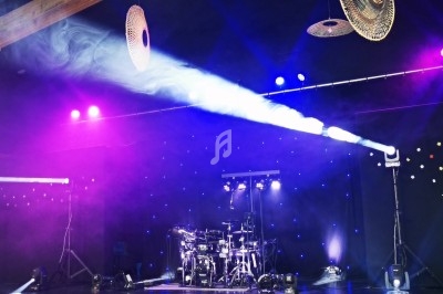 Scène de concert avec batterie éclairée par des projecteurs colorés et un fond étoilé lumineux.