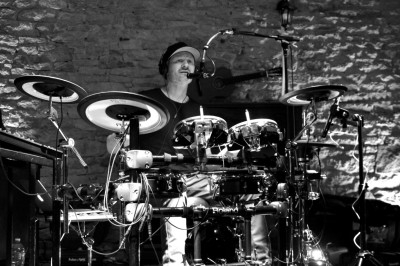 Un musicien joue de la batterie électronique dans un cadre en pierre, avec un micro et un éclairage tamisé.