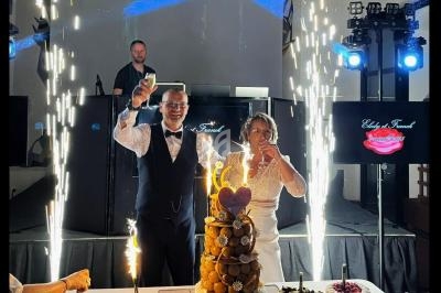 Un couple célèbre son mariage devant une pièce montée illuminée par des étincelles, entouré de desserts.