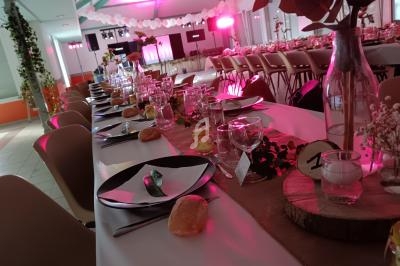 Grande table de réception décorée avec vaisselle, fleurs et éclairage rose dans une salle festive.