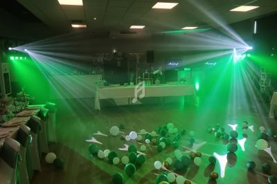 Salle de réception décorée avec des ballons au sol, éclairée par des lumières vertes et des projecteurs.