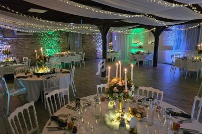 Salle de réception décorée avec des guirlandes lumineuses, des tables dressées et un éclairage coloré.