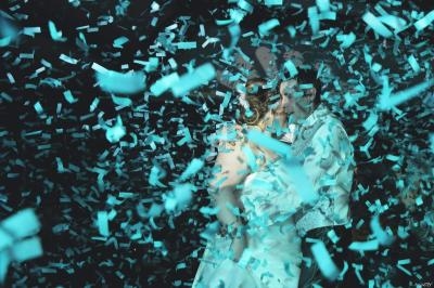 Un couple danse entouré de confettis bleus tombant dans une ambiance festive et lumineuse.