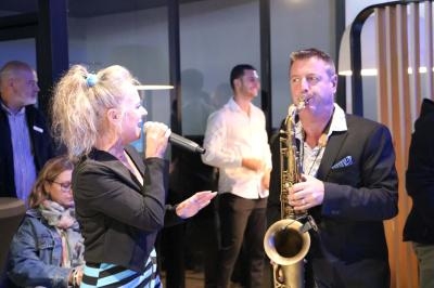 Une chanteuse et un saxophoniste jouent de la musique lors d'un événement en intérieur, entourés de spectateurs.