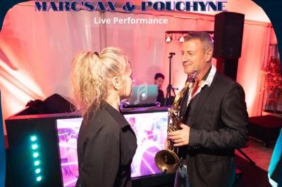 Un homme tenant un saxophone échange avec une femme devant une scène avec un DJ en arrière-plan.