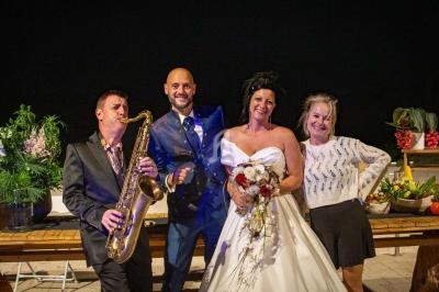 Un groupe de personnes posant lors d'une soirée, avec une mariée en robe blanche et un musicien jouant du saxophone.