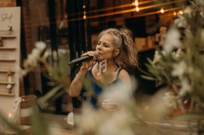 Femme chantant au micro dans un espace intérieur décoré de lumières et de plantes.