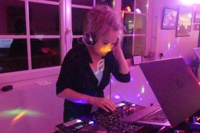 Une femme mixe de la musique sur une console DJ dans une pièce éclairée par des lumières colorées.