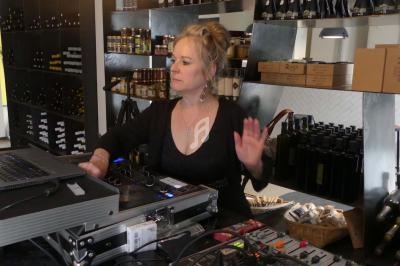 Femme utilisant un équipement de mixage audio dans un magasin avec des étagères remplies de bouteilles et de produits.