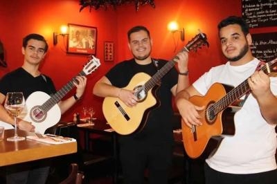 Trois musiciens jouent de la guitare dans un restaurant à l'ambiance chaleureuse avec des murs rouges.