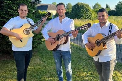 Trois hommes jouent de la guitare acoustique dans un jardin, vêtus de chemises blanches et entourés de verdure.