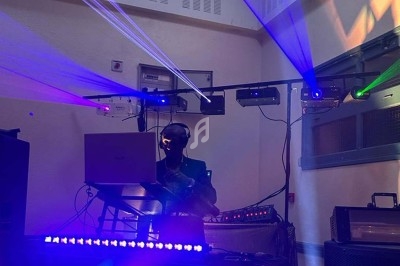 Un DJ mixe derrière son ordinateur, entouré de lumières colorées et d'équipements audio dans une salle sombre.