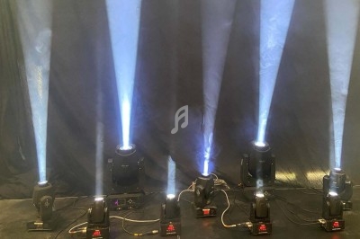 Projecteurs lumineux diffusant des faisceaux blancs sur un fond sombre, alignés sur une scène ou un espace intérieur.