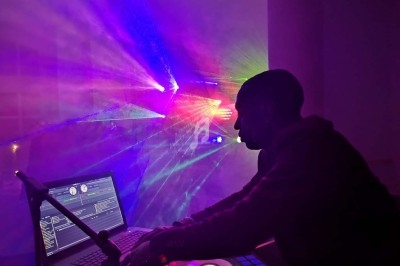 Un DJ mixe sur une console devant un ordinateur, éclairé par des faisceaux lumineux colorés dans une ambiance sombre.