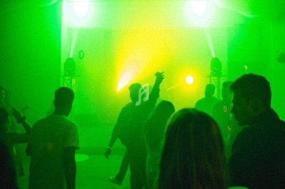 Personnes dansant dans une salle éclairée par des lumières vertes et jaunes, créant une ambiance festive.