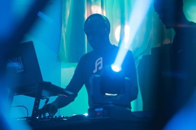 Un DJ mixant sur une scène éclairée par des lumières bleues, avec un projecteur lumineux au premier plan.