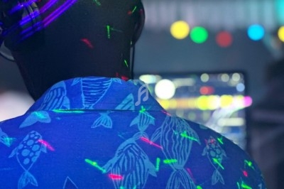 Homme de dos portant une chemise à motifs de poissons, éclairé par des lumières colorées dans une ambiance festive.