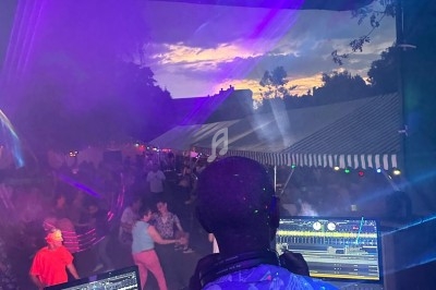 Un DJ mixant en plein air au coucher du soleil, avec une foule dansante et des jeux de lumière colorés.